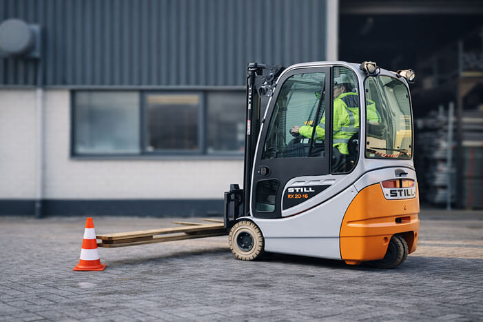 Operator in a high-visibility vest driving a forklift during training on a manoeuvring yard.